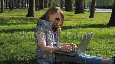 一个带着笔记本电脑的十几岁女孩。 公园里的女孩在用笔记本电脑工作。 手拿手镯。